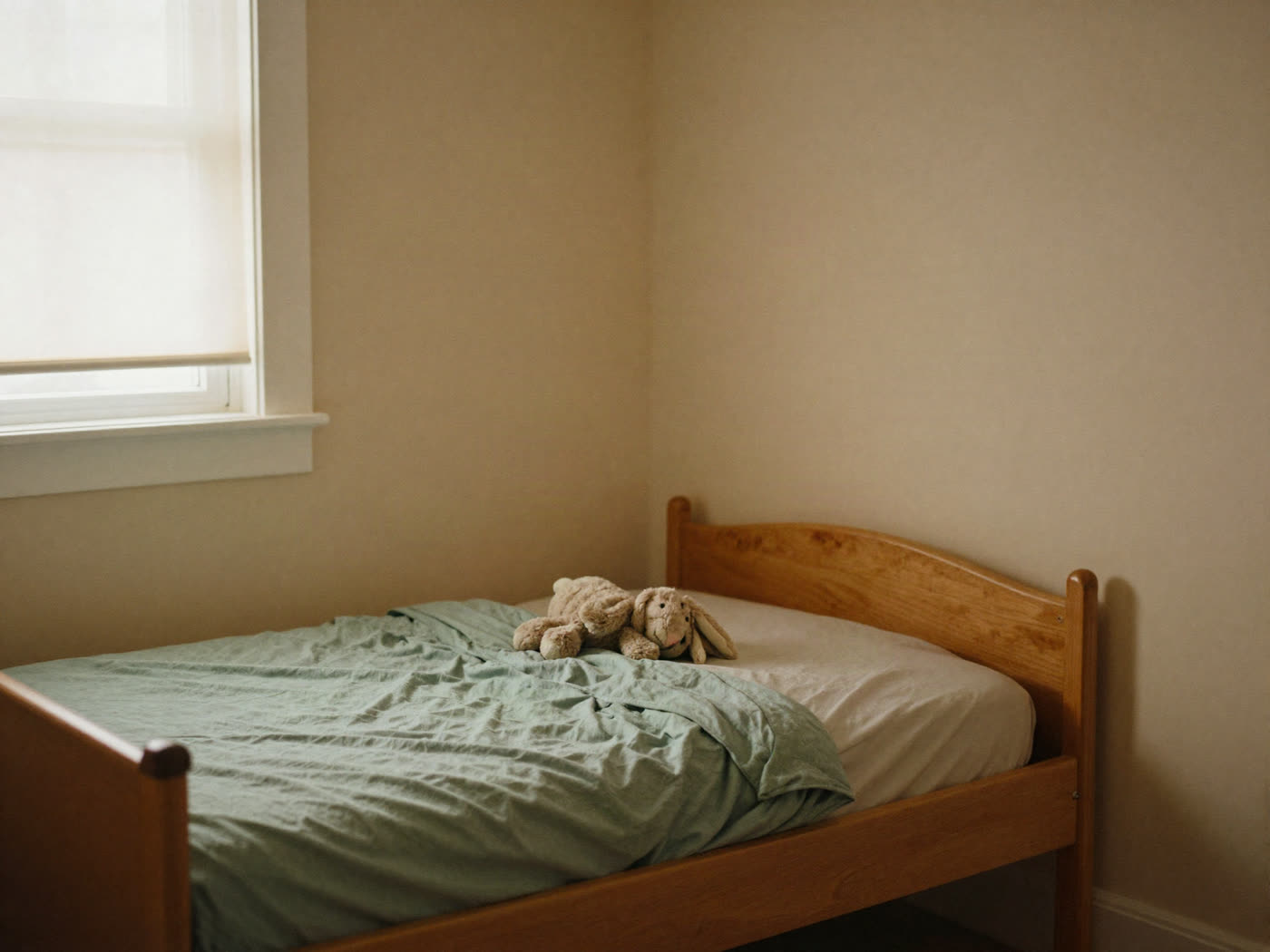 A darkened bedroom with one band of daylight across a folded blanket on a low bed.